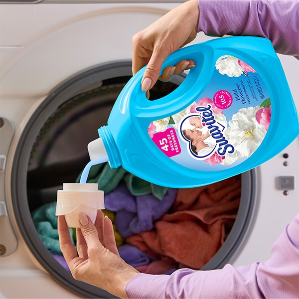 Pouring Suavitel Field Flowers fabric conditioner into cap in front of laundry machine.